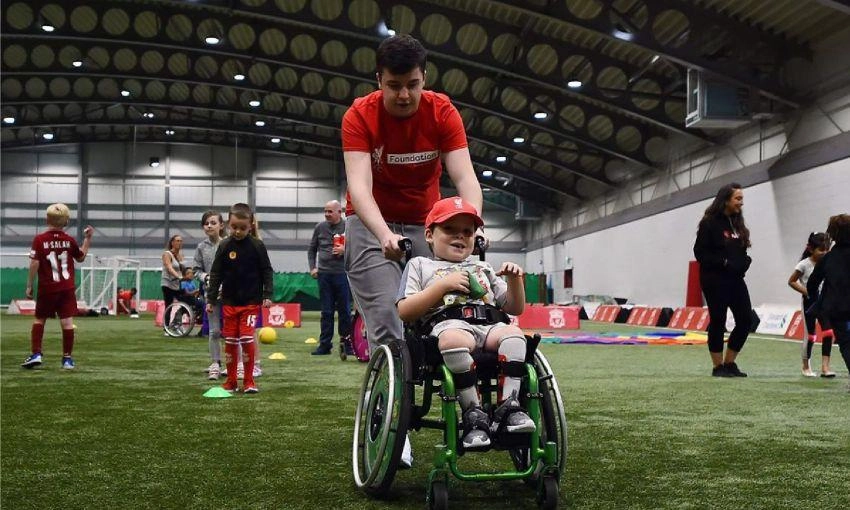 Boy being pushed in a wheelchair, smiling, inside a sports hall by a Foundation volunteer