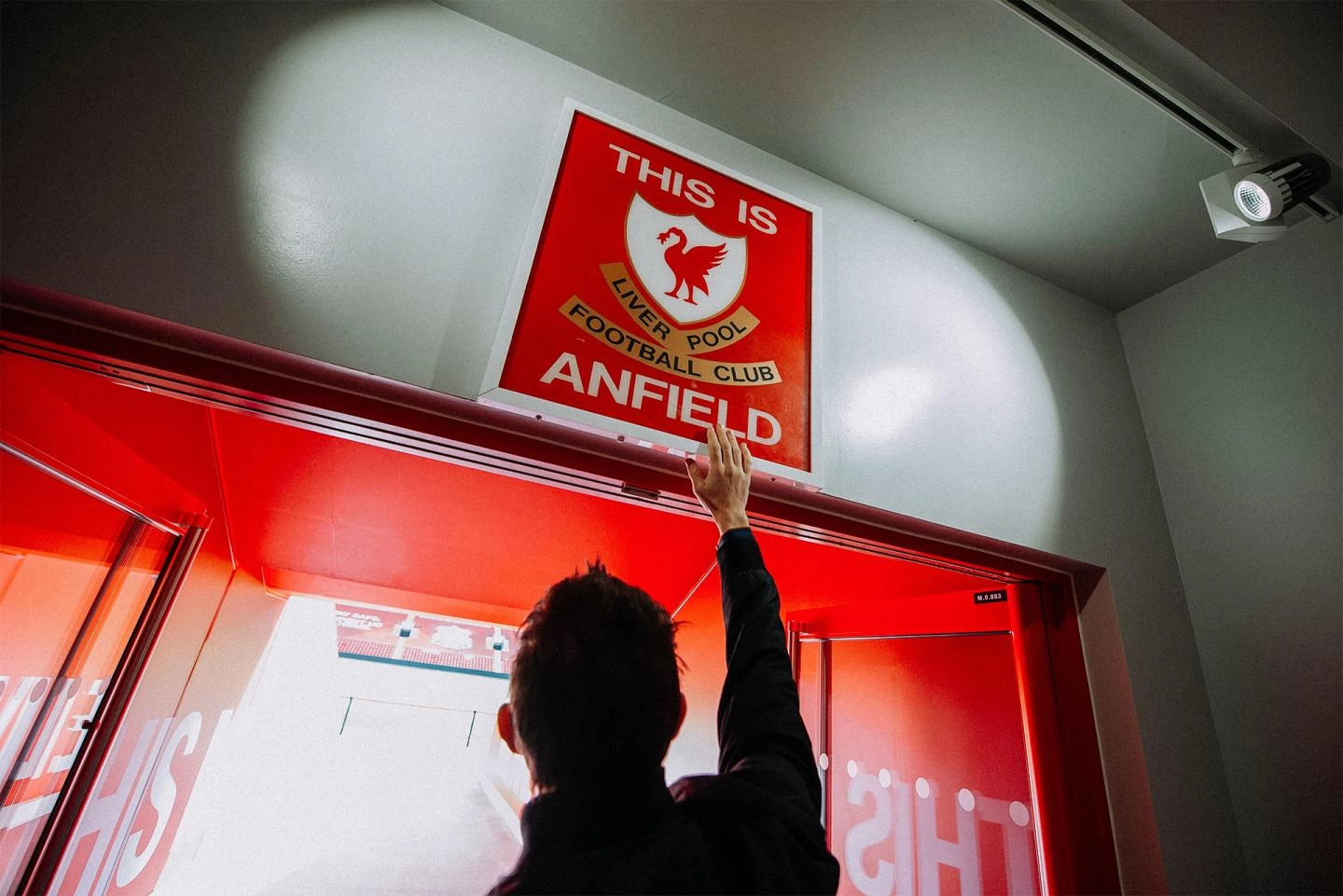 Person reaching up and touching the This is Anfield sign with his hand