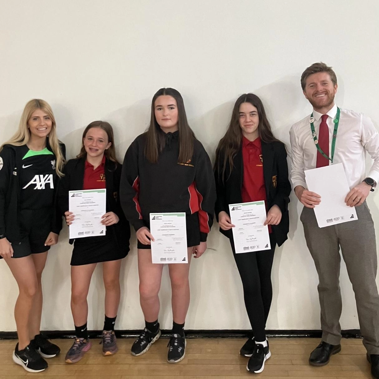 LFC Foundation coach, three students and a teacher holding certificates in a gym