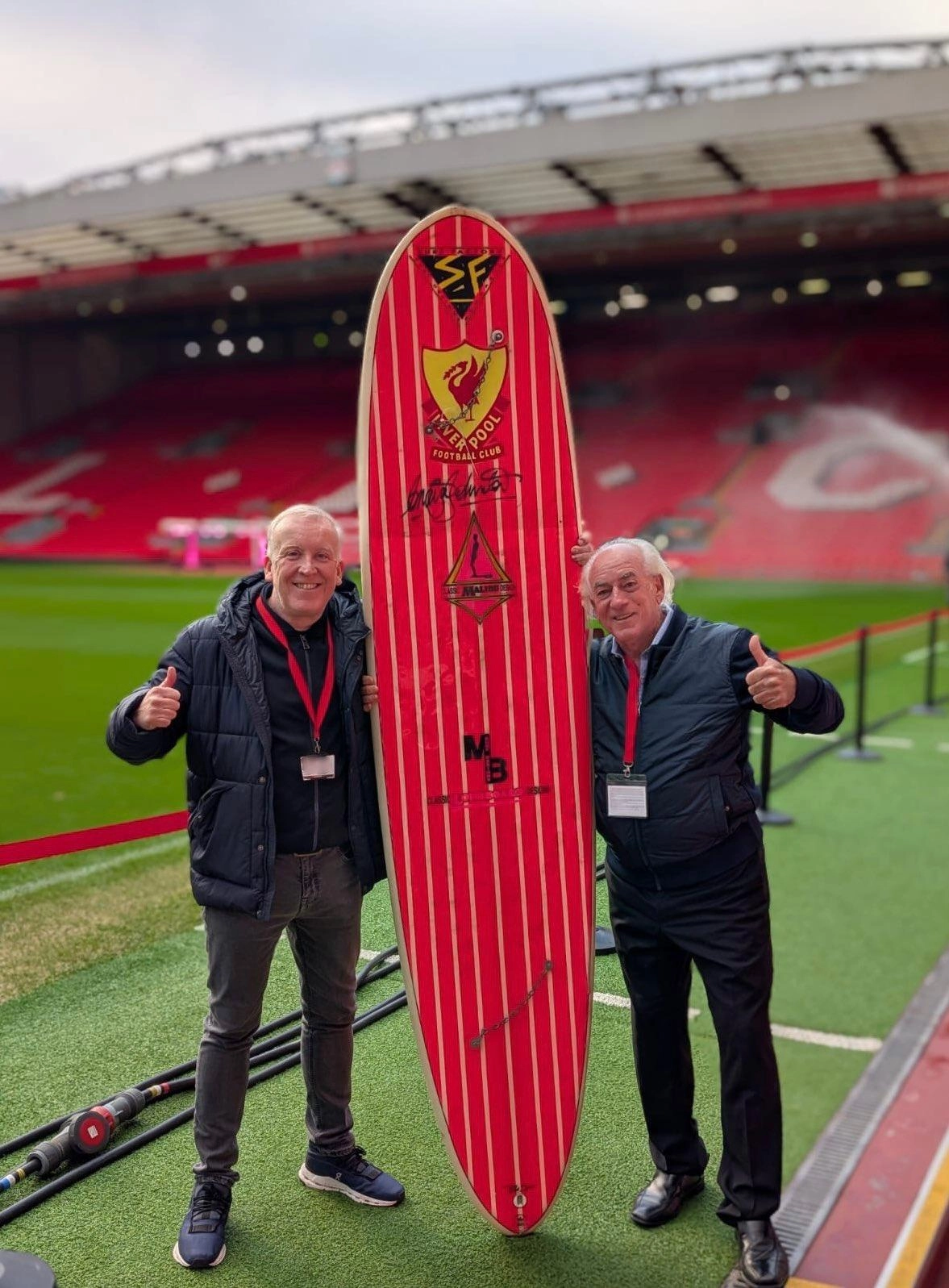 Johnston (right) with the surfboard at Anfield, alongside LFC curator Mark Platt