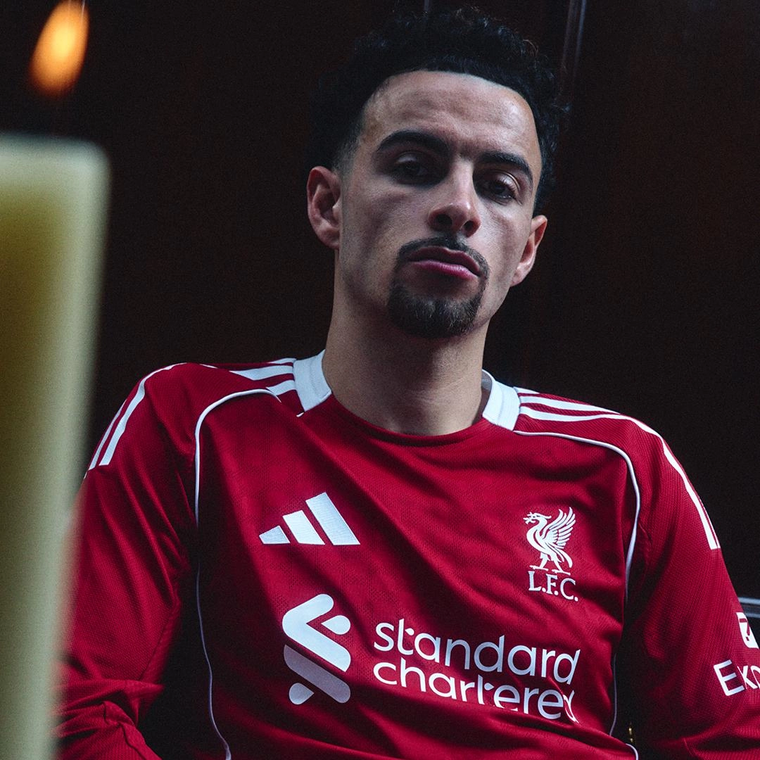Jogador do Liverpool vestindo a camisa titular adidas 25/26 vermelha, detalhes brancos