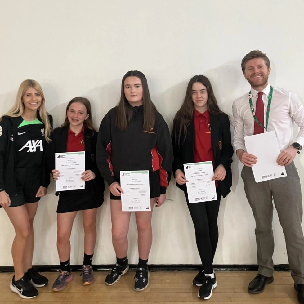 LFC Foundation coach, three students and a teacher holding certificates in a gym